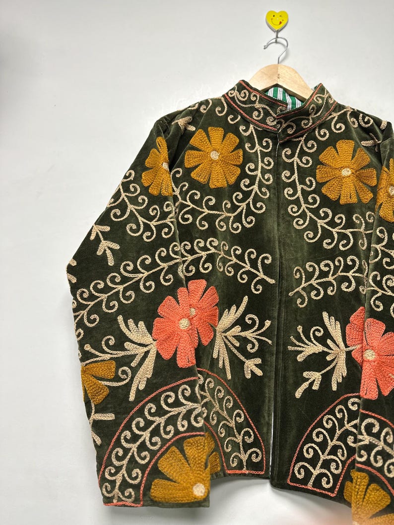 May include: Dark green velvet jacket with intricate floral embroidery in shades of gold, orange, and cream. The jacket features a high collar and a full-length zipper. The floral design includes large flowers and swirling vines, creating a detailed and ornate look.