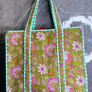 May include: A green quilted tote bag with a floral print and white and green gingham trim. The bag has two long handles.