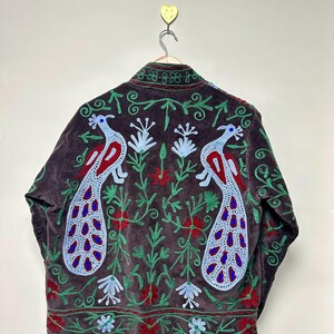 May include: A dark brown jacket with embroidered peacock and floral designs. The jacket features a high collar and is adorned with red, blue, and green embroidery. The peacock design is prominently displayed on the back.