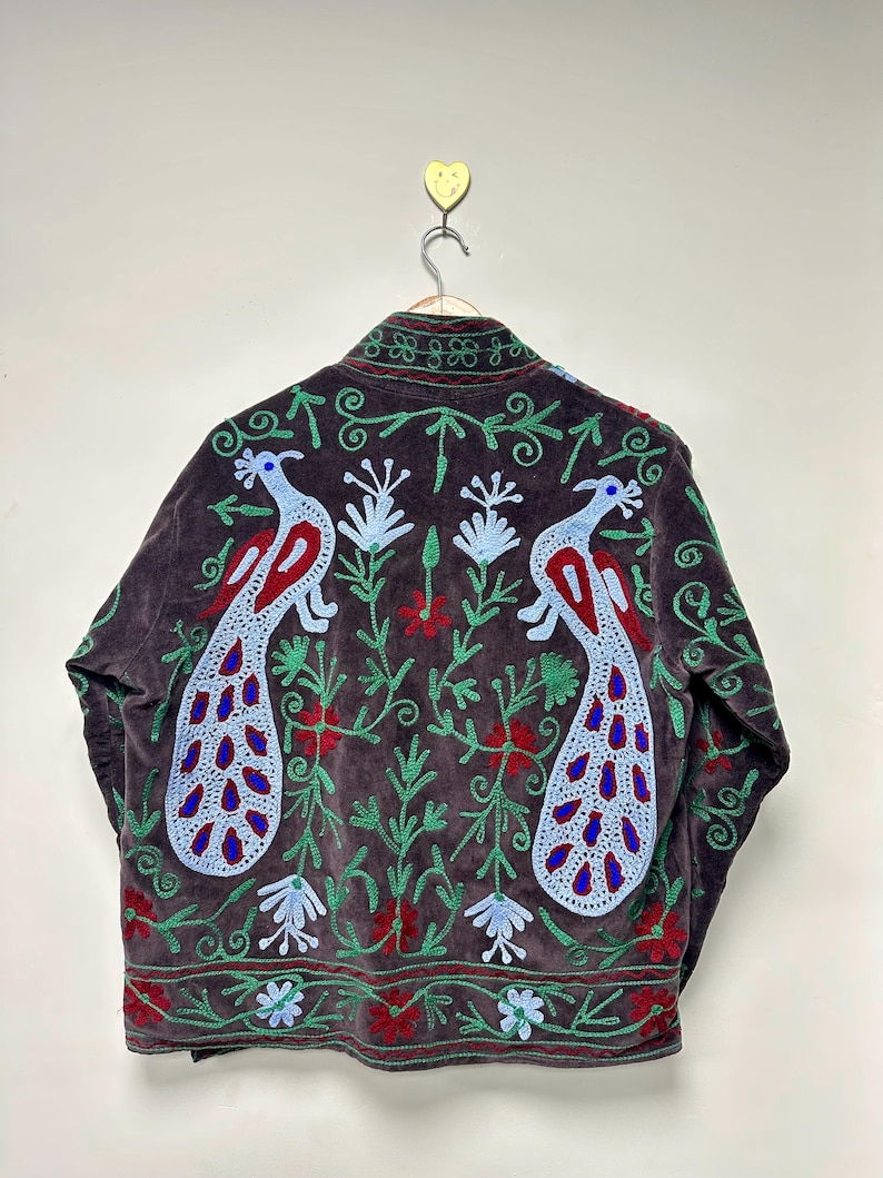 May include: A dark brown jacket with embroidered peacock and floral designs. The jacket features a high collar and is adorned with red, blue, and green embroidery. The peacock design is prominently displayed on the back.