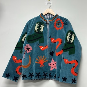 May include: Teal velvet jacket with embroidered designs. Features include green cowboy boots, orange snakes, pink flowers, and black star accents. The jacket has a zip closure and a striped collar.