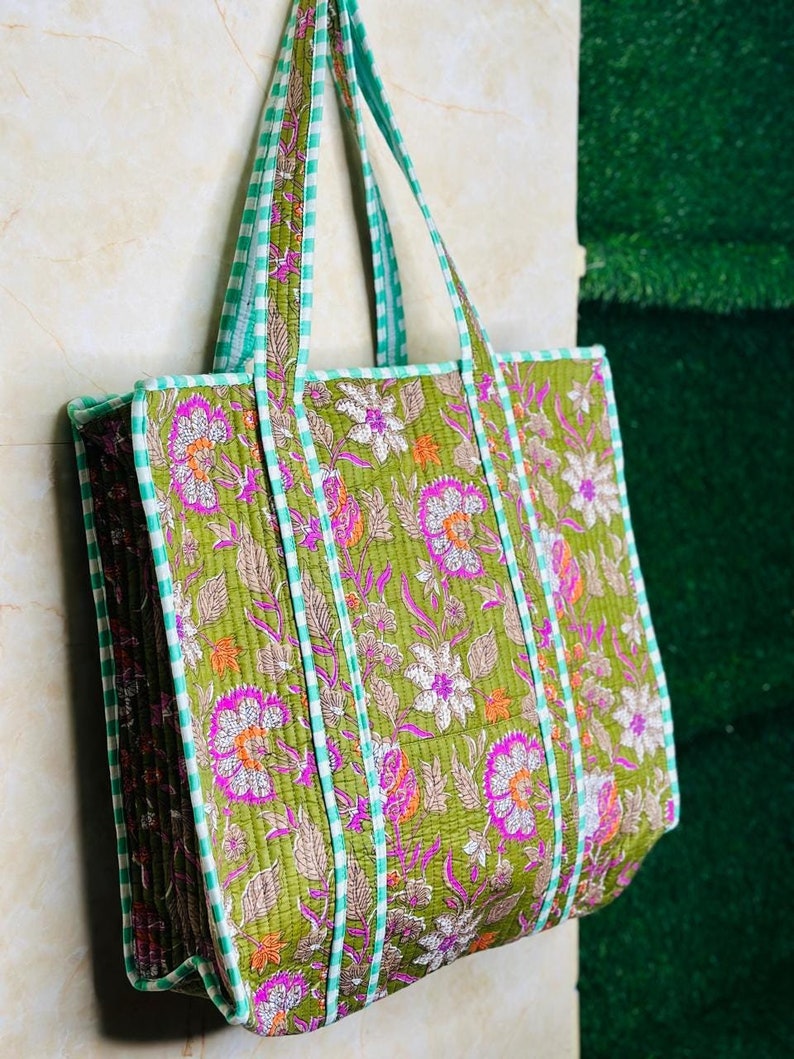 May include: A green quilted tote bag with a floral print and white and green striped trim. The bag has two handles.