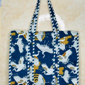 May include: A blue tote bag with white and gold crane print. The bag has white and blue striped straps.
