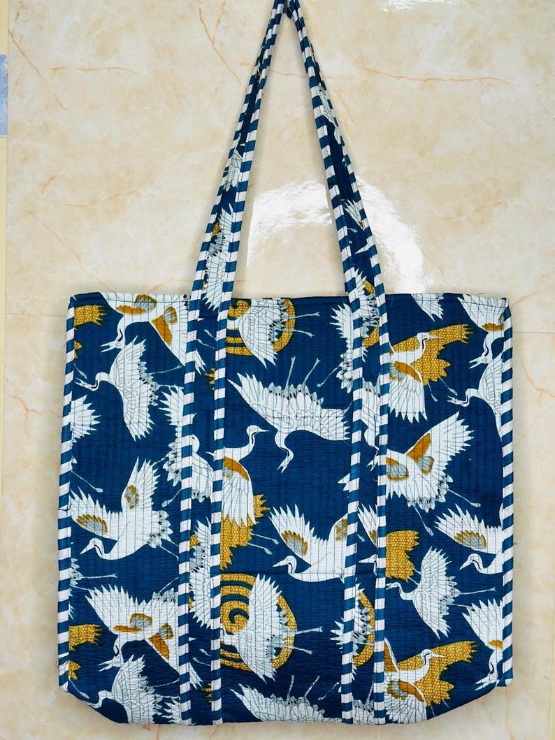 May include: A blue tote bag with white and gold crane print. The bag has white and blue striped straps.