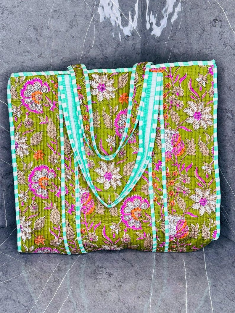 May include: A green quilted tote bag with a floral print and white and green striped handles.