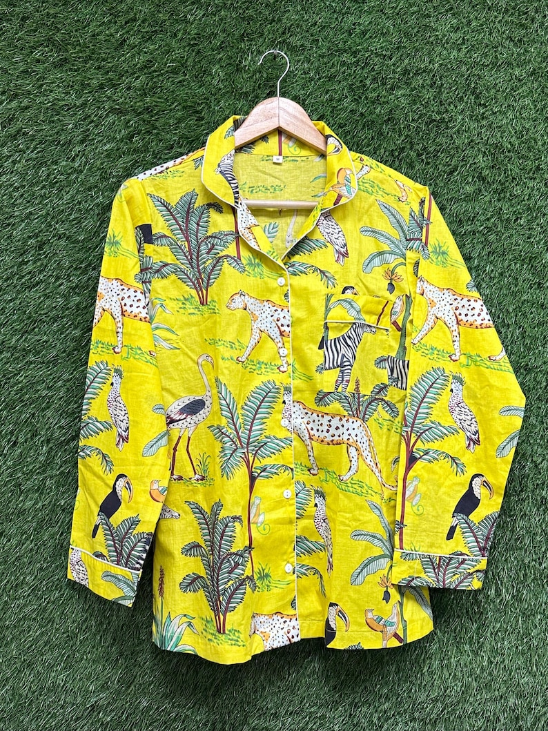 Puede incluir: Camisa amarilla con botones y un estampado de jungla vibrante. El dise&ntilde;o presenta leopardos, cebras, tucanes y palmeras. La camisa tiene mangas largas y ribete blanco en los pu&ntilde;os y el cuello.