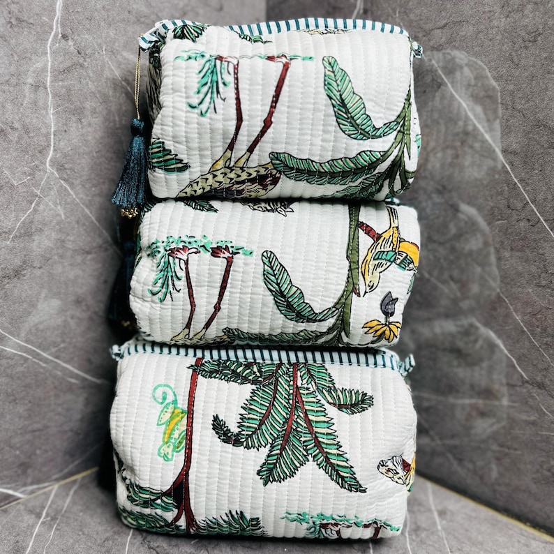 May include: Three white quilted fabric pouches with a green, brown, and yellow tropical print. The pouches have a teal and white striped trim.