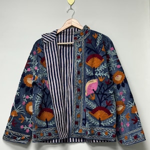 May include: A blue jacket featuring vibrant floral embroidery in shades of orange, pink, and dark red. The garment has long sleeves, a straight hem, and an open front that reveals a contrasting interior lining with a navy and white vertical stripe pattern.