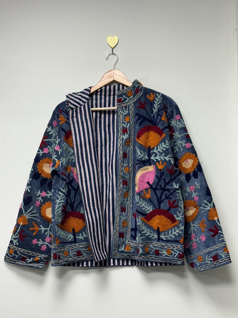 May include: A blue jacket featuring vibrant floral embroidery in shades of orange, pink, and dark red. The garment has long sleeves, a straight hem, and an open front that reveals a contrasting interior lining with a navy and white vertical stripe pattern.