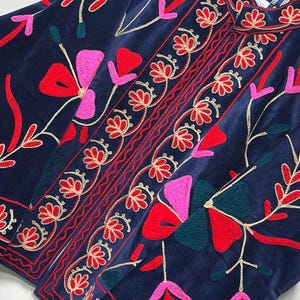 Op de afbeelding: Een marineblauw fluwelen jasje met levendig bloemenborduursel in tinten rood, roze en donkergroen. Het kledingstuk is voorzien van een mandarijnkraag, een knoopsluiting aan de voorzijde en een gestreepte voering zichtbaar bij de halslijn.
