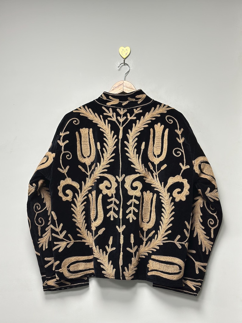 May include: A black jacket featuring intricate gold-coloured embroidery in a floral and tulip pattern. The garment has a high collar, long sleeves, and a central vertical seam, showcasing detailed stitching across the entire back surface.