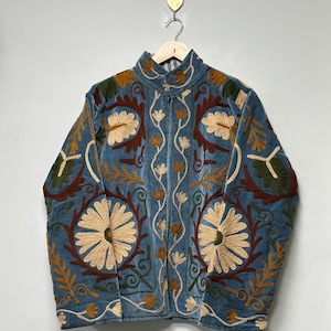 May include: A blue velvet jacket featuring intricate embroidery in cream, dark brown, and olive green. The design includes large floral motifs, scrolling vines, and leaf patterns across the front and sleeves, with a high collar and long sleeves.