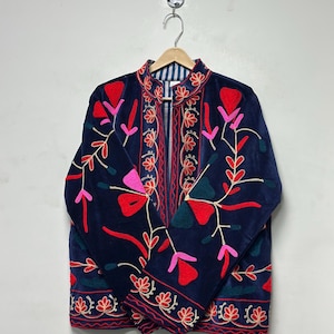 Op de afbeelding: Een donkerblauw fluwelen jasje met levendige bloemenborduursels in rood, roze en petrol. Het jasje heeft een mandarijnkraag, lange mouwen en een gestreepte voering, met symmetrische botanische patronen op de voorpanden van het kledingstuk.