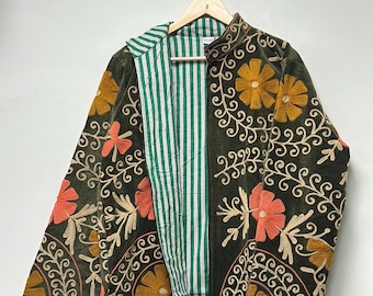 Puede incluir: Chaqueta de terciopelo verde oscuro con bordados florales en naranja, dorado y beige. La chaqueta tiene un forro a rayas verdes y blancas y está colgada en una percha de madera.