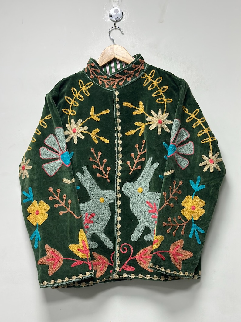 May include: A dark green velvet jacket featuring a high collar and intricate embroidery. The design includes two light blue rabbits facing each other, surrounded by colorful floral and leaf patterns in yellow, blue, and pink thread.