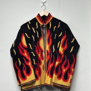 May include: Black jacket with embroidered flames in red, yellow, and orange. The jacket has a striped lining at the bottom and a collar with yellow embroidery. The jacket is hanging on a wooden hanger.
