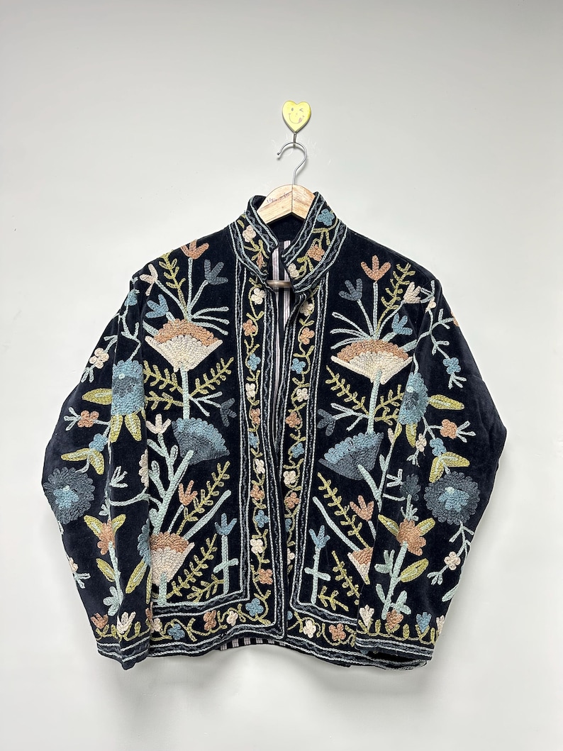 May include: A dark navy blue jacket with intricate floral embroidery in shades of beige, blue, and green. The jacket features a high collar and a zip-up front. The embroidery is detailed and covers the front and sleeves.