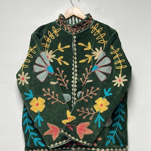 May include: A dark green velvet jacket featuring a high collar and long sleeves. The jacket is decorated with vibrant, multi-colored floral and leaf embroidery in shades of yellow, light blue, pink, and brown, with a striped lining visible at the neck.
