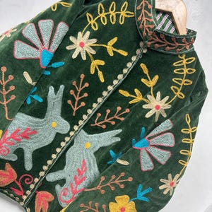 May include: A dark green velvet jacket featuring intricate multi-colored embroidery of rabbits, flowers, and leaves. The garment has a high collar, long sleeves, and a front opening with a decorative stitched border and a striped inner lining.