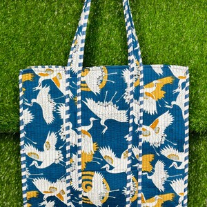 May include: A blue tote bag with a white and yellow crane pattern. The bag has white and blue striped handles.