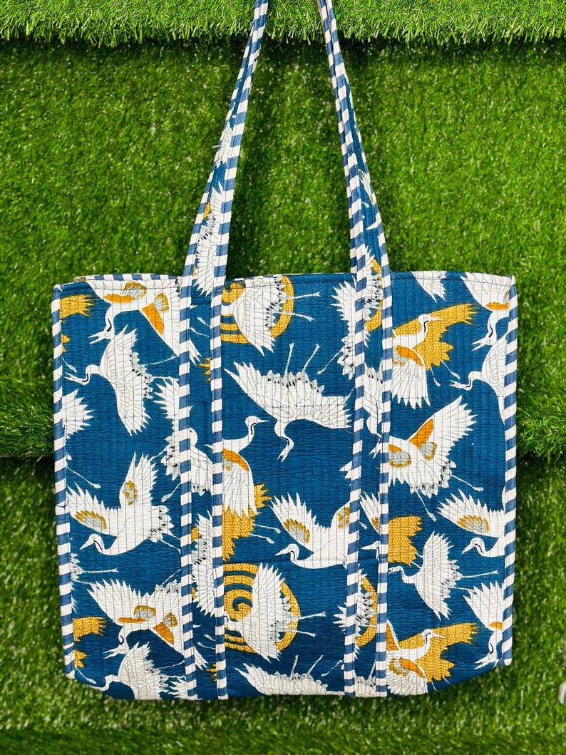 May include: A blue tote bag with a white and yellow crane pattern. The bag has white and blue striped handles.