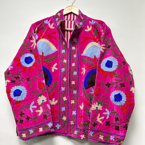 K&ouml;nnte beinhalten: Eine leuchtend pinkfarbene Jacke mit aufwendigen, mehrfarbigen Blumenstickereien. Das Design umfasst gro&szlig;e blaue und rote kreisf&ouml;rmige Bl&uuml;tenmotive, gr&uuml;ne St&auml;ngel und zarte Blattmuster. Sie hat einen Stehkragen und lange &Auml;rmel.