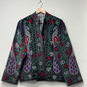 May include: A dark gray velvet jacket featuring intricate embroidery of two large peacocks facing each other. The design includes vibrant red flowers, green leafy vines, and silver-toned peacock feathers with blue accents. The jacket has a high collar.