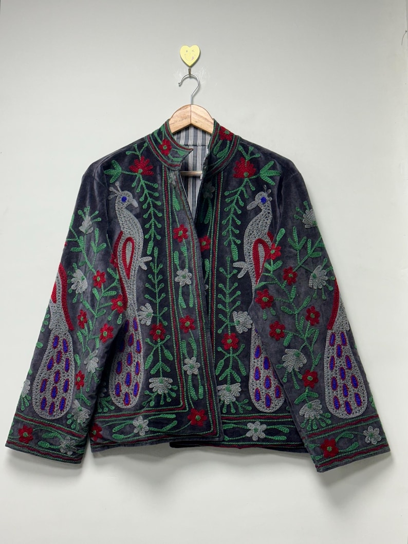 May include: A dark gray velvet jacket featuring intricate embroidery of two large peacocks facing each other. The design includes vibrant red flowers, green leafy vines, and silver-toned peacock feathers with blue accents. The jacket has a high collar.