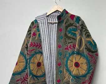 May include: A long-sleeve jacket featuring a grey base with vibrant floral embroidery in yellow, teal, and magenta. The jacket has a high collar, a front zip closure, and an interior lining made of a white and grey vertical striped fabric.