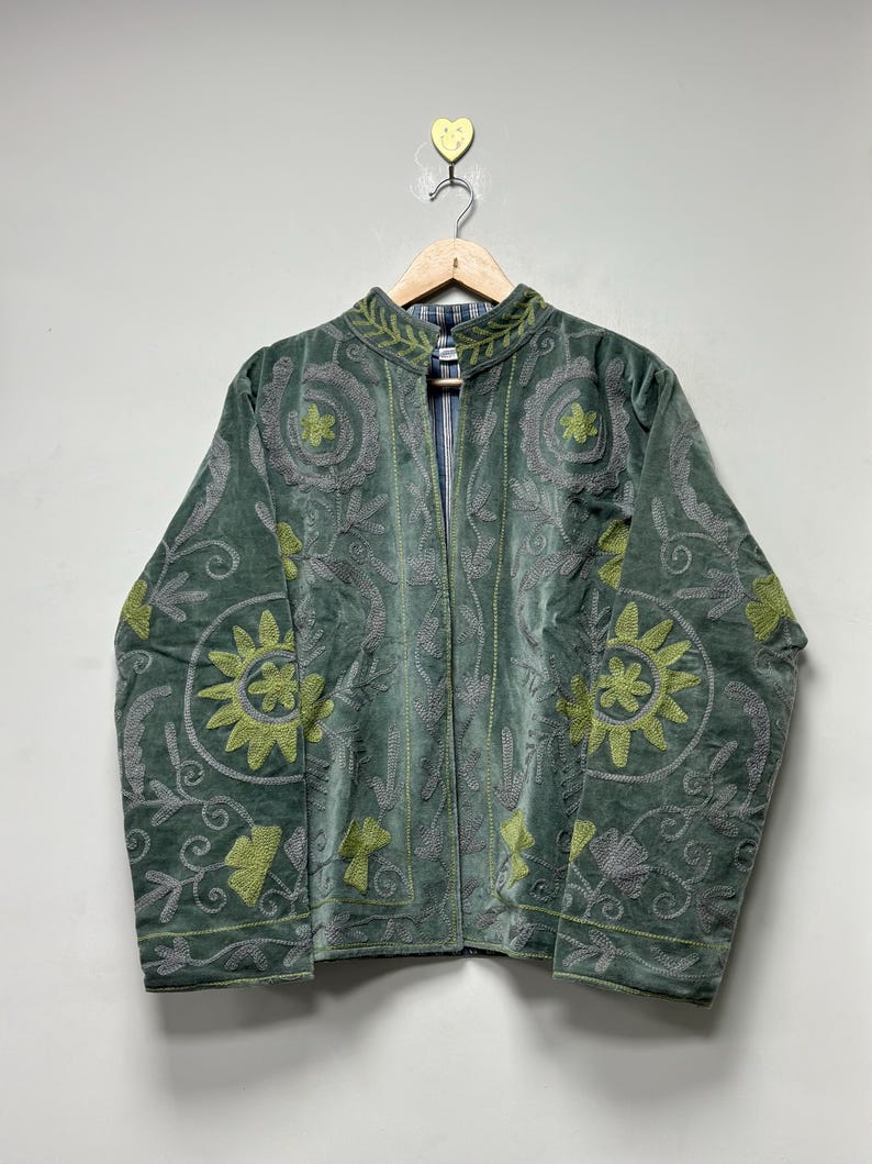 May include: A green velvet jacket with intricate floral embroidery in gray and lime green. The jacket has a mandarin collar and a striped lining. It is displayed on a wooden hanger.