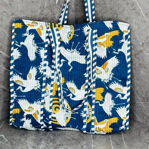 May include: A blue and white quilted tote bag with a pattern of white cranes on a blue background. The bag has white and blue striped straps.