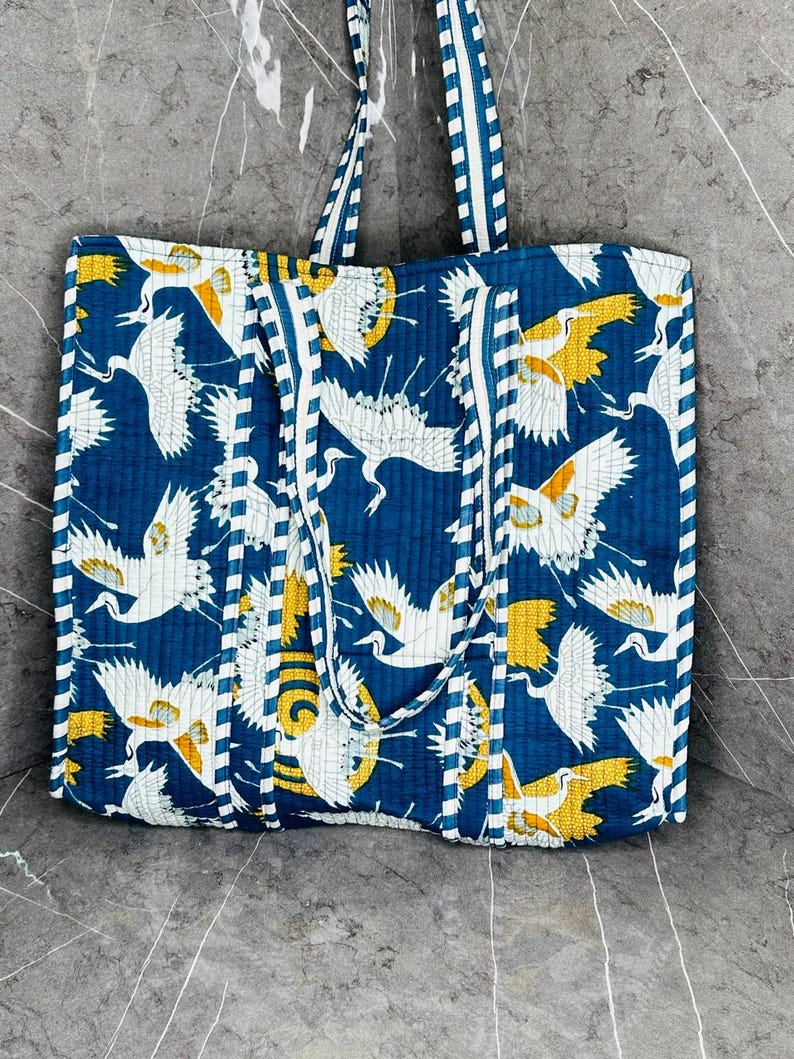May include: A blue and white quilted tote bag with a pattern of white cranes on a blue background. The bag has white and blue striped straps.