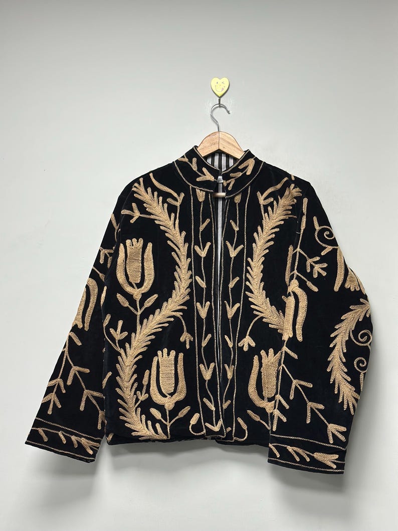 May include: A black jacket featuring long sleeves, a high collar, and an open front. The garment is decorated with intricate gold-coloured embroidery depicting stylised floral and leaf patterns across the front and sleeves on a dark fabric.
