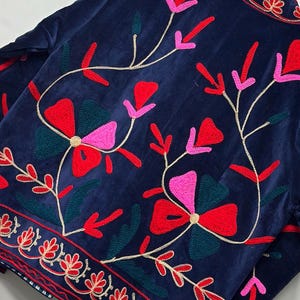 Op de afbeelding: Een marineblauw fluwelen jasje met levendig bloemenborduursel in tinten rood, roze en donkergroen. Het ontwerp bevat gestileerde bloemmotieven en kronkelende stengels, met een decoratieve geborduurde rand langs de onderzoom.