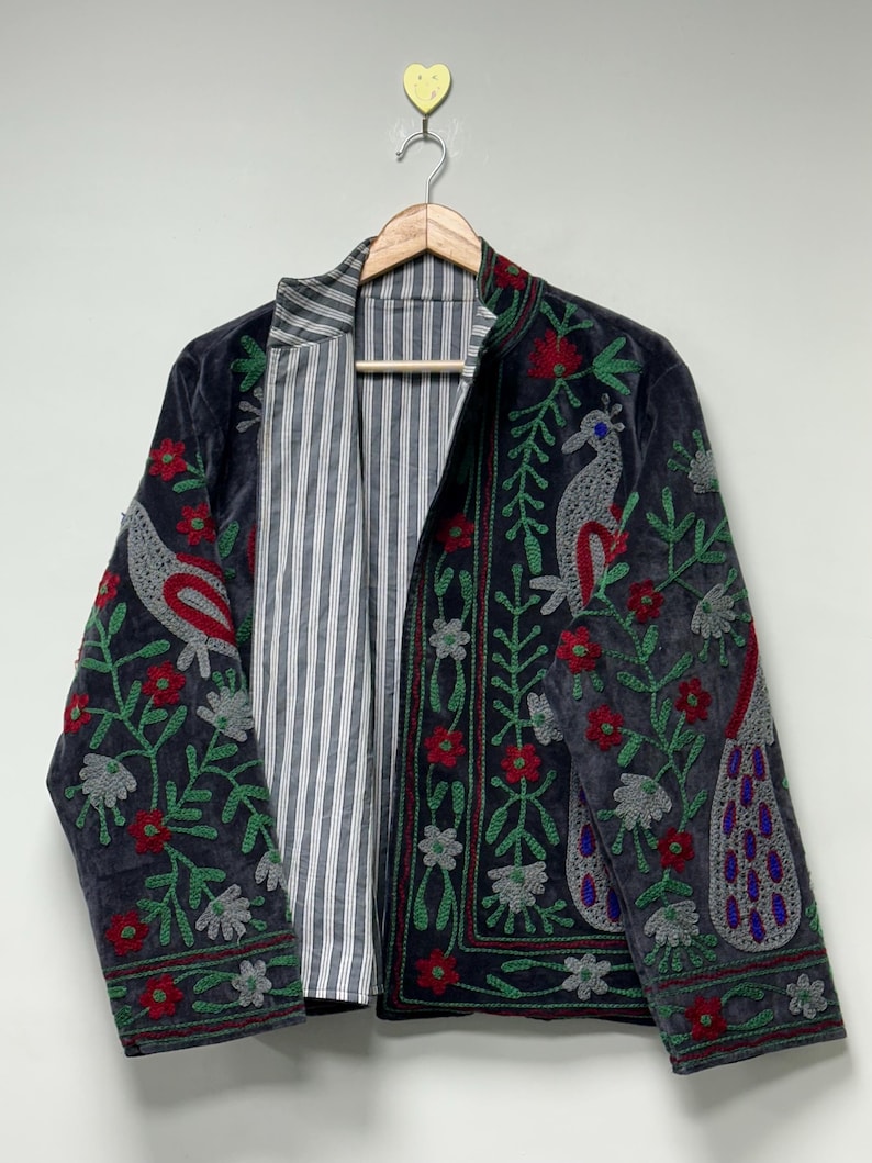 May include: A dark gray jacket featuring intricate embroidery of birds and floral patterns in red, green, and gray. The jacket has a stand-up collar and a contrasting interior lining with a vertical white and gray pinstripe design.