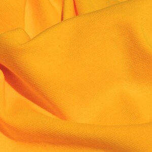 May include: Close-up of a bright yellow fabric with a textured surface. The fabric is folded and draped, creating soft folds and curves.