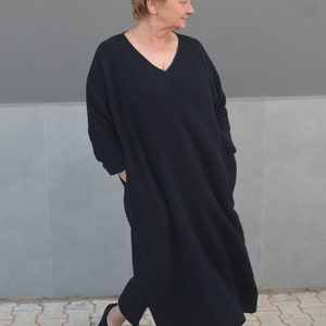 Puede incluir: Un vestido negro de manga larga con cuello en V. El vestido est&aacute; hecho de una tela suave y texturizada y tiene un corte holgado.