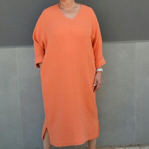 Puede incluir: Un vestido largo de color naranja coral holgado con cuello en V y mangas 3/4. El vestido tiene una abertura lateral y est&aacute; hecho de una tela suave y texturizada.