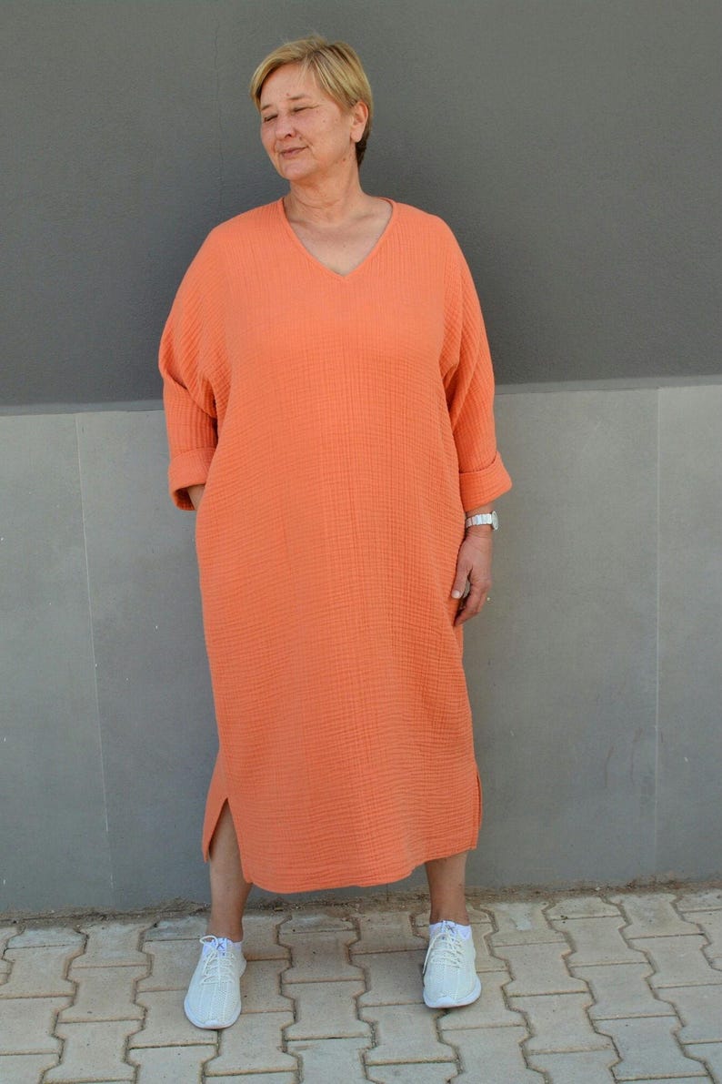 Puede incluir: Un vestido largo de color naranja coral holgado con cuello en V y mangas 3/4. El vestido tiene una abertura lateral y est&aacute; hecho de una tela suave y texturizada.