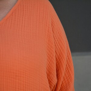 Puede incluir: Primer plano de una camisa de algod&oacute;n naranja brillante texturizada con cuello en V.