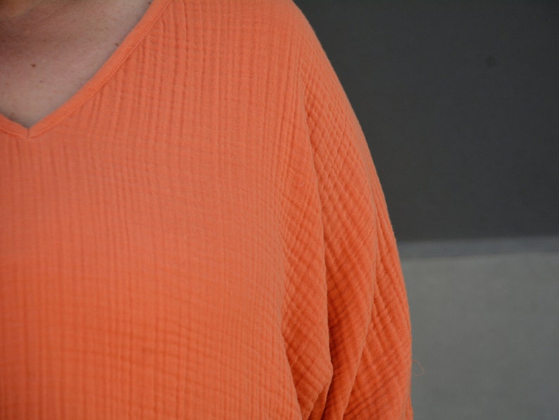 Puede incluir: Primer plano de una camisa de algod&oacute;n naranja brillante texturizada con cuello en V.