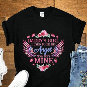 May include: Black t-shirt with a pink and blue graphic design. The graphic features a pair of angel wings with the text "Daddy's Girl I used to be his Angel Now he's Mine".