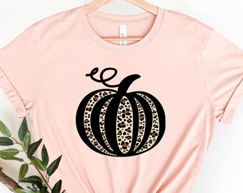 May include: A pink t-shirt with a black and brown leopard print pumpkin graphic. The pumpkin has a black stem and a curly vine.