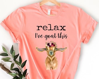 May include: A peach colored t-shirt with the text "relax I've goat this" in black. A watercolor illustration of a goat wearing a flower crown is below the text.