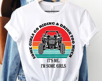 Puede incluir: Camiseta blanca con un gráfico en blanco y negro de un vehículo side-by-side con un fondo de puesta de sol. El texto dice "Some girls go riding & drink too much. It's me. I'm some girls."