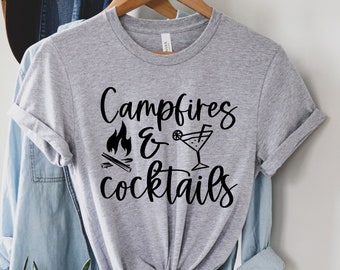 May include: A gray t-shirt with the text "Campfires & Cocktails" in black lettering. The text is stylized with a campfire and a cocktail glass graphic.