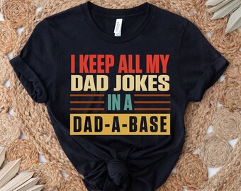 May include: Black t-shirt with a vintage-style graphic that says "I keep all my dad jokes in a dad-a-base".
