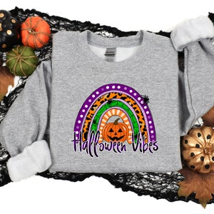 May include: A gray sweatshirt with a rainbow design featuring a pumpkin, spiders, and the text "Halloween Vibes".