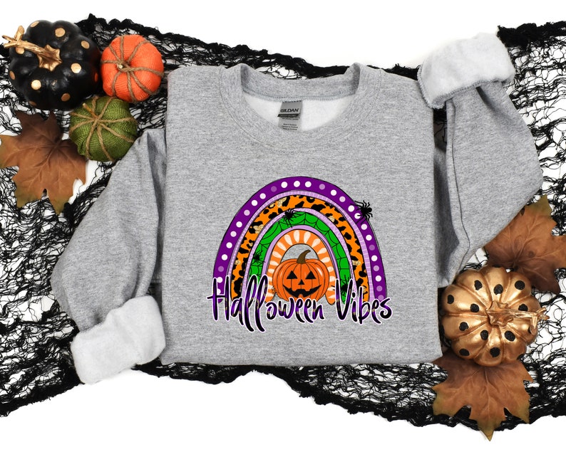 May include: A gray sweatshirt with a rainbow design featuring a pumpkin, spiders, and the text "Halloween Vibes".