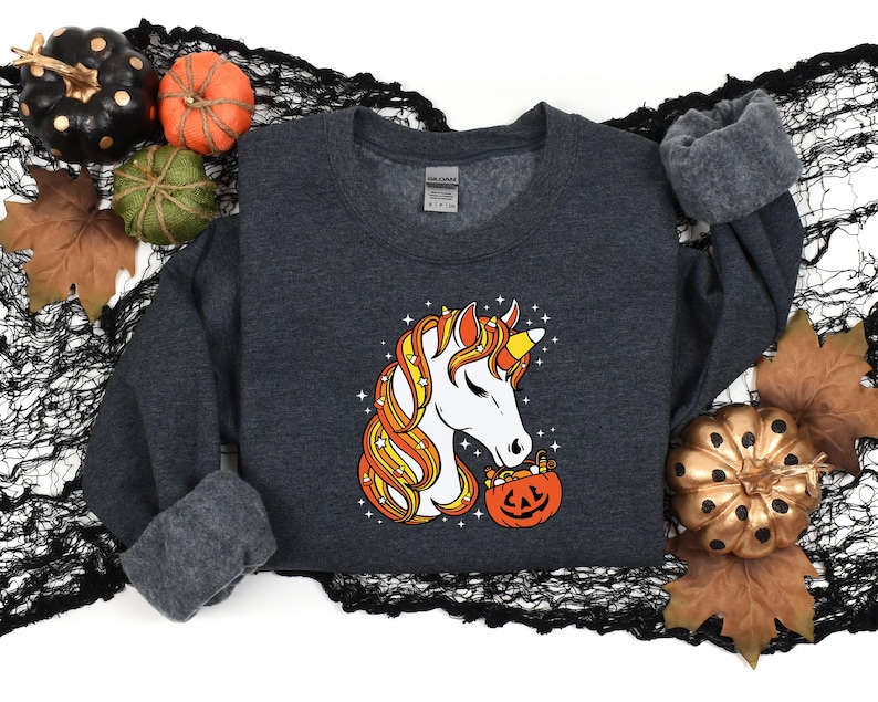 May include: A dark gray sweatshirt with a white unicorn holding a candy corn filled pumpkin. The unicorn has a yellow and orange mane and tail.